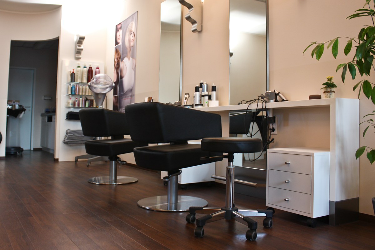Schwarze Salonstühle vor hohen Spiegeln und hellen Ablagen